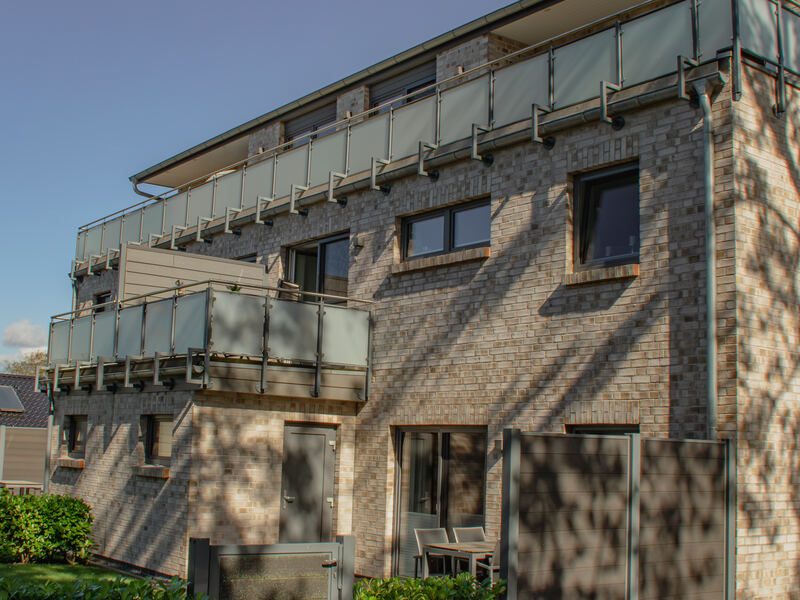 Rückseite des Hauses mit Balkonen, Terrasse und Hecke im Abendlicht
