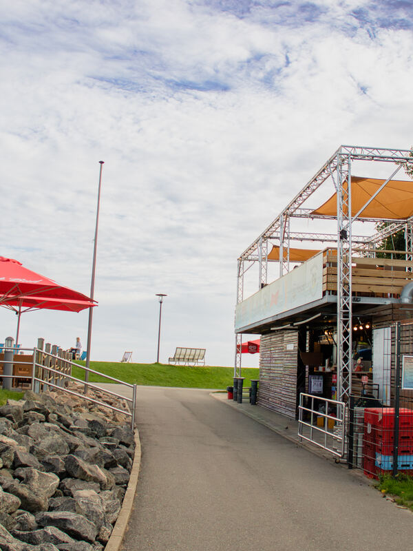 Kiosk mit Terrasse und Sonnenschirmen an der Badestelle hinterm Deich