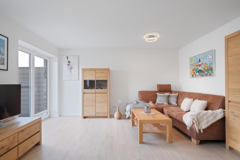 Helles Wohnzimmer mit Sofa, Fernseher und Balkontür